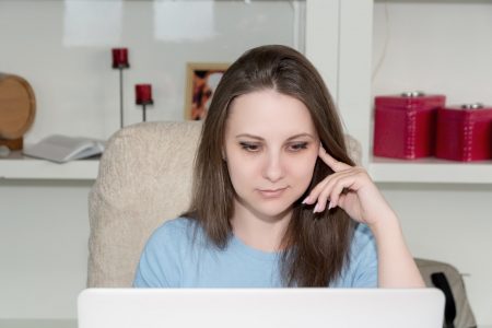 mulher de camiseta azul na frente do laptop pensando (Bermix Studio)