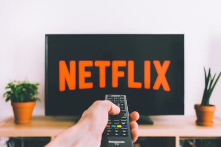 Pessoa segurando controle remoto com TV na Netflix (freestocks)
